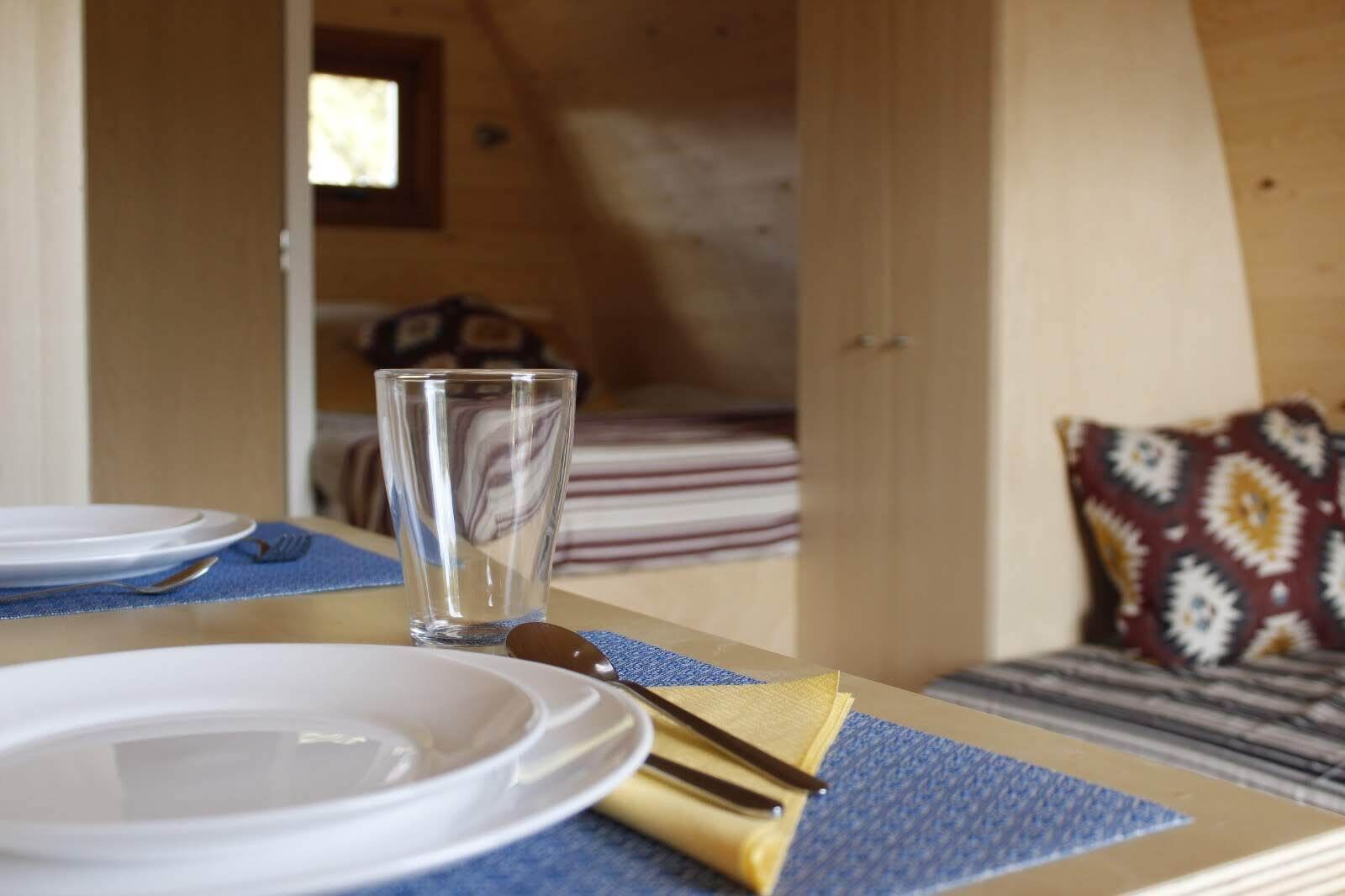 Una mesa de comedor ordenada con platos, cubiertos y una copa en el interior acogedor de una cabaña.