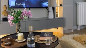 Un salon moderne doté d’un téléviseur à écran plat diffusant une vidéo musicale, d’une table basse ronde agrémentée d’objets décoratifs, d’un canapé et d’une bibliothèque pourvue d’un éclairage d’ambiance.