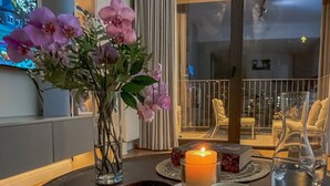 Une table ronde avec une bougie, un vase de fleurs et un plateau contenant des bols et un verre d’eau.
