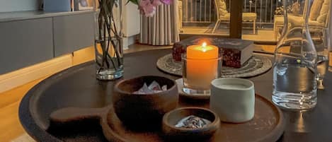 A round table with a candle, a vase of flowers, and a tray with bowls and a glass of water.