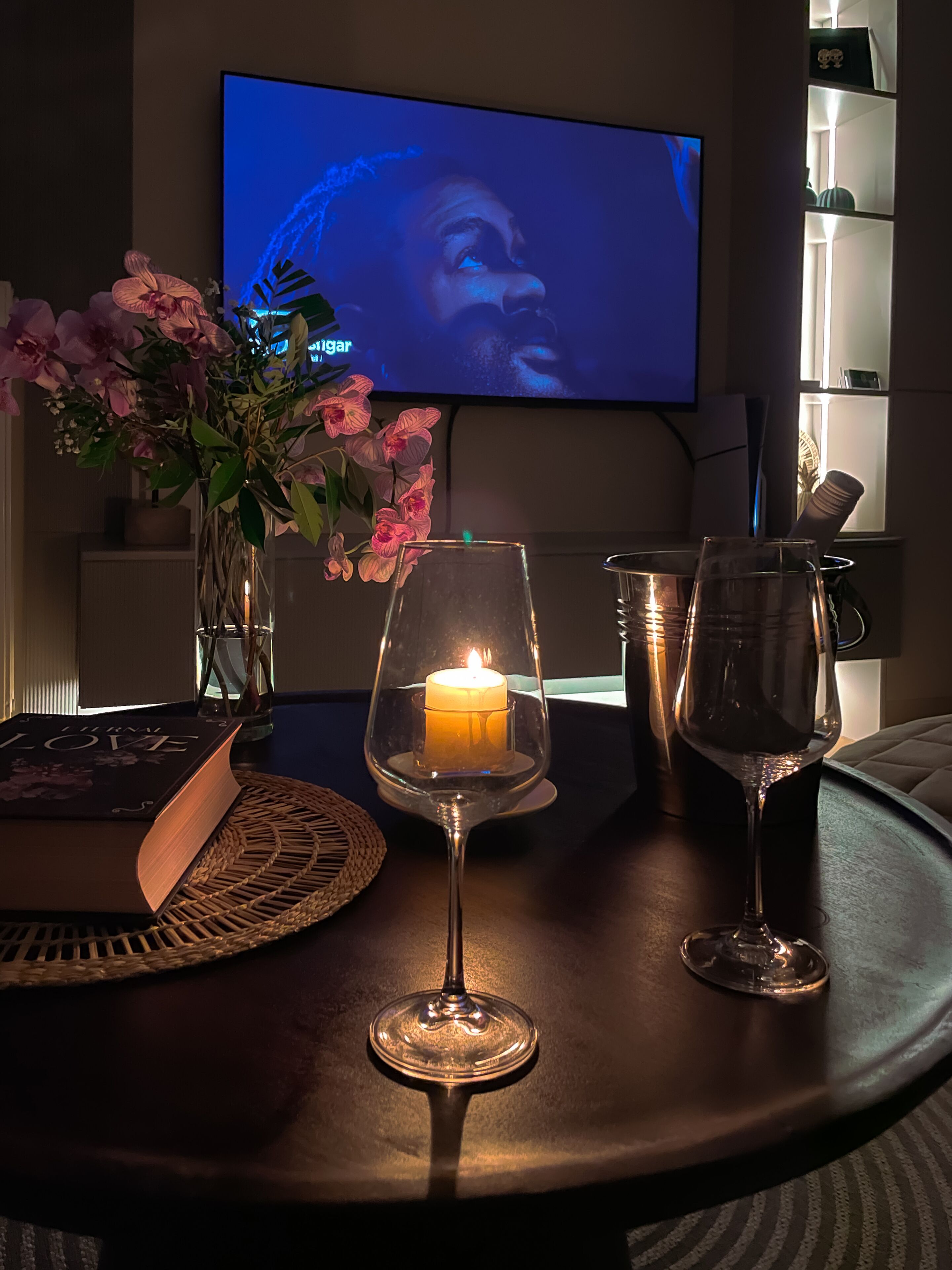Una habitación acogedora con televisión, una vela en un candelabro y un florero con flores sobre una mesa.