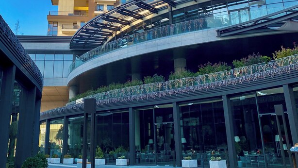 Un bâtiment moderne doté d’une façade en verre incurvée, d’espaces extérieurs aménagés pour s’asseoir et d’un jardin sur le toit.