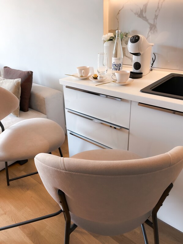 Une cuisine moderne avec un plan de travail blanc, une machine à café et un vase rempli de fleurs.