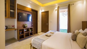 A hotel room with a bed, a TV mounted on the wall, a wooden cabinet, and a door leading to a balcony. - Alaya Stays BYDM The Sky Heaven - 4 BHK Penthouse 15 Min from Triveni Ghat With Balcony & Lift (Rishikesh)