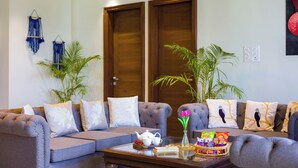 A modern living room with a grey sofa, decorative pillows, a coffee table with a teapot, books, and snacks. There are two large wooden doors and potted plants. - Alaya Stays BYDM The Sky Heaven - 4 BHK Penthouse 15 Min from Triveni Ghat With Balcony & Lift (Rishikesh)