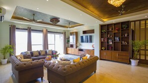 A spacious living room with a large sofa set, a television, and a wooden cabinet with shelves. - Alaya Stays BYDM The Sky Heaven - 4 BHK Penthouse 15 Min from Triveni Ghat With Balcony & Lift (Rishikesh)