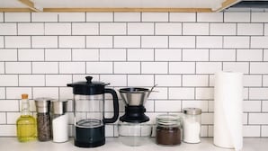 A kitchen with white cabinets, a coffee maker, and various containers. - Studio Downtown+HighFalls+Kitchen+TV+Unity_Pet. (Rochester)
