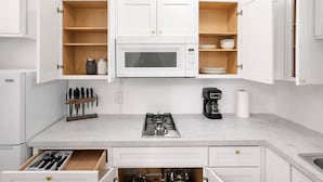 A kitchen with white cabinets, a microwave, a gas stove, a coffee maker, and a knife block. - Your Cozy Studio HighFalls TV Kitchen Rochest DT (Rochester)
