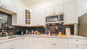 A modern kitchen with white cabinetry, a black tiled backsplash, and stainless steel appliances. - Your Cozy_Studio_HighFalls_TV+Kitchen+Rochest_DT (Rochester)