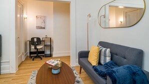 A modern living room with a grey sofa, a wooden coffee table, and a black office chair. - Your Cozy_Studio_HighFalls_TV+Kitchen+Rochest_DT (Rochester)