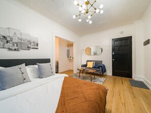 A modern bedroom with a large bed, a sofa, a coffee table, and a cityscape artwork on the wall. - Your Cozy_Studio_HighFalls_TV+Kitchen+Rochest_DT (Rochester)
