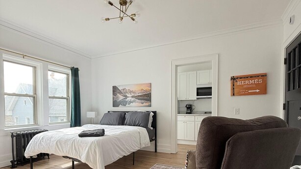 A modern bedroom with a bed, a chair, a rug, and a painting on the wall. - Modern studio in Downtown Rochester with a full kitchen and Smart TV, steps from High Falls. (Rochester)
