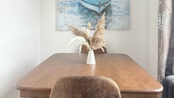 Een eethoek met een houten tafel, een stoel, een schilderij van een boot en pampa's in een vaas.