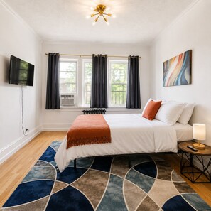 Ein Schlafzimmer mit einem Bett, einem Fernseher, einem Fenster mit Vorhängen, einer Heizung und einem Bild an der Wand.