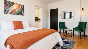 A hotel room with a bed, a green armchair, a small table, a mirror, and a ceiling light fixture. - Studio Near Downtown+Wi-Fi+Queenbd_HighFall. (Rochester)