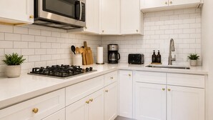 A modern kitchen with white cabinetry, a stainless steel microwave, a gas stove, a coffee maker, and a toaster. - Studio Near Downtown+Wi-Fi+Queenbd_HighFall. (Rochester)