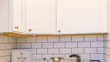 A kitchen with white cabinets, a tiled backsplash, a coffee maker, a glass carafe, a toaster, and a sign that reads "You had me at."