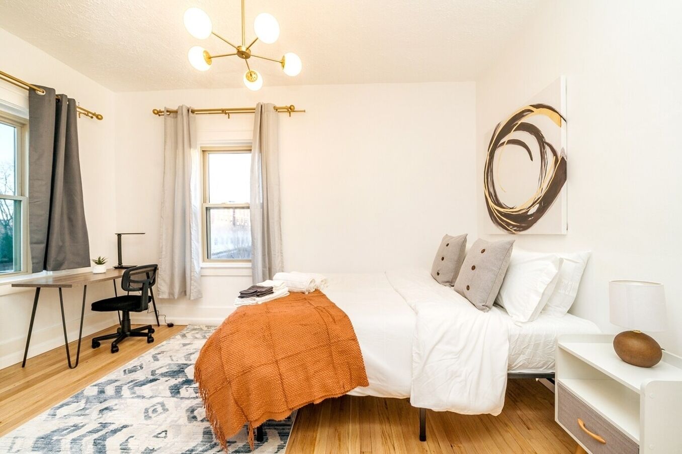 Un dormitorio moderno con cama, escritorio, silla y un ventanal con cortinas.