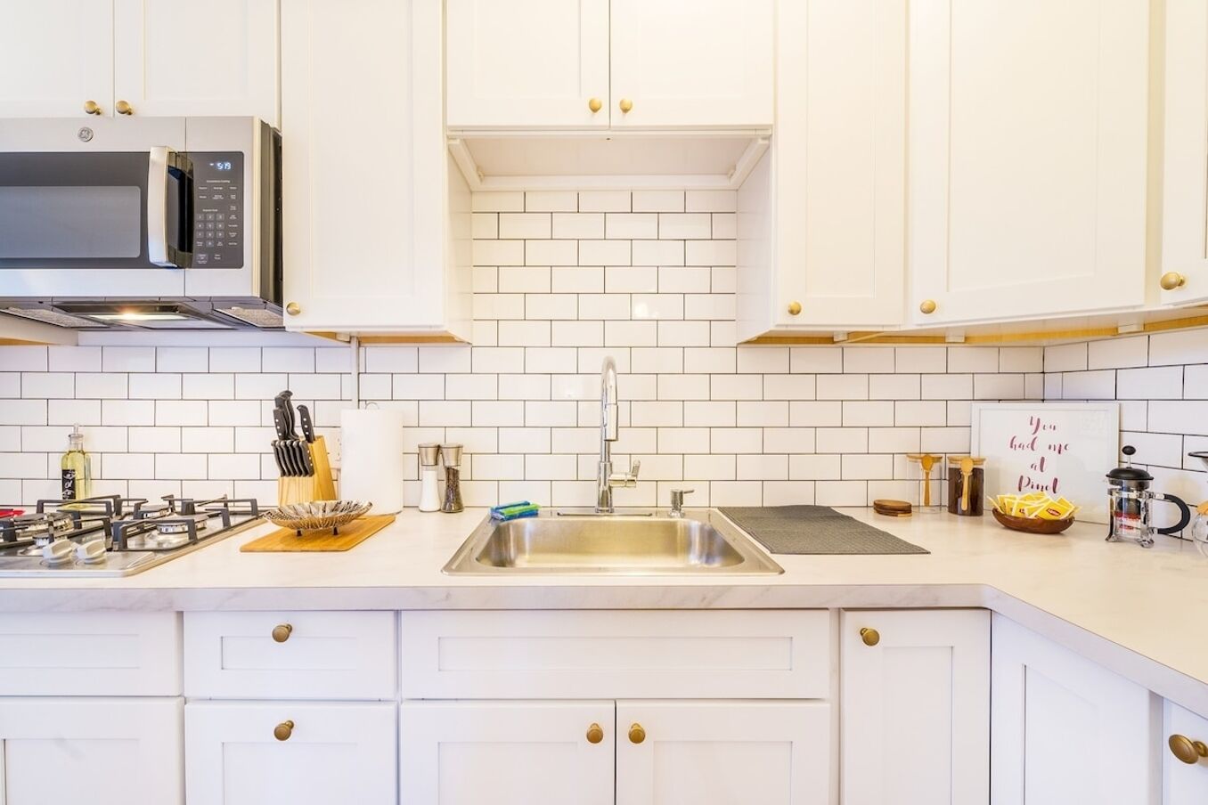 Une cuisine moderne avec des meubles blancs, un évier en acier inoxydable et un four à micro-ondes.