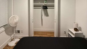 Ett sovrum med en säng, en fläkt, ett element och ett litet bord med en lampa.