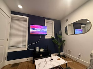 A room with a TV mounted on the wall, a round mirror, a table with a marble top, and a potted plant. - Cornhill Apt w_FreeParking_Kitchen_W+D (Rochester)