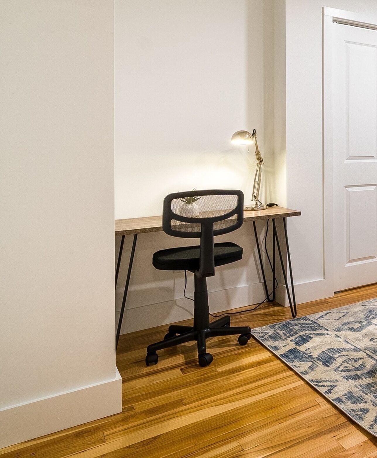 Ein Arbeitsbereich mit Schreibtisch, Stuhl, Lampe und einem gemusterten Teppich.