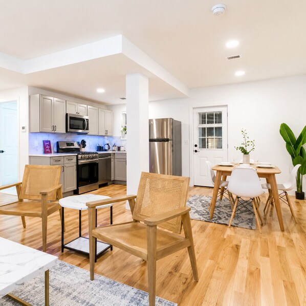 A modern kitchen with stainless steel appliances, a dining area with a table and chairs, and a large plant.