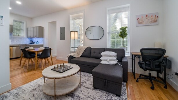 A modern living room with a sofa, a dining table with chairs, a coffee table, and a desk with a chair. - Cornhill 2BDRM-HighFall+EquippedKitchen+Wi-Fi (Rochester)