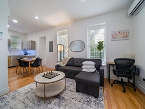 A modern living room with a sofa, a dining table with chairs, a coffee table, and a desk with a chair.