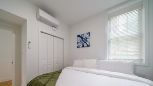 A bedroom with a large bed, white walls, a window with blinds, a door, and a wall-mounted air conditioner. - Cornhill 2BDRM-HighFall+EquippedKitchen+Wi-Fi (Rochester)