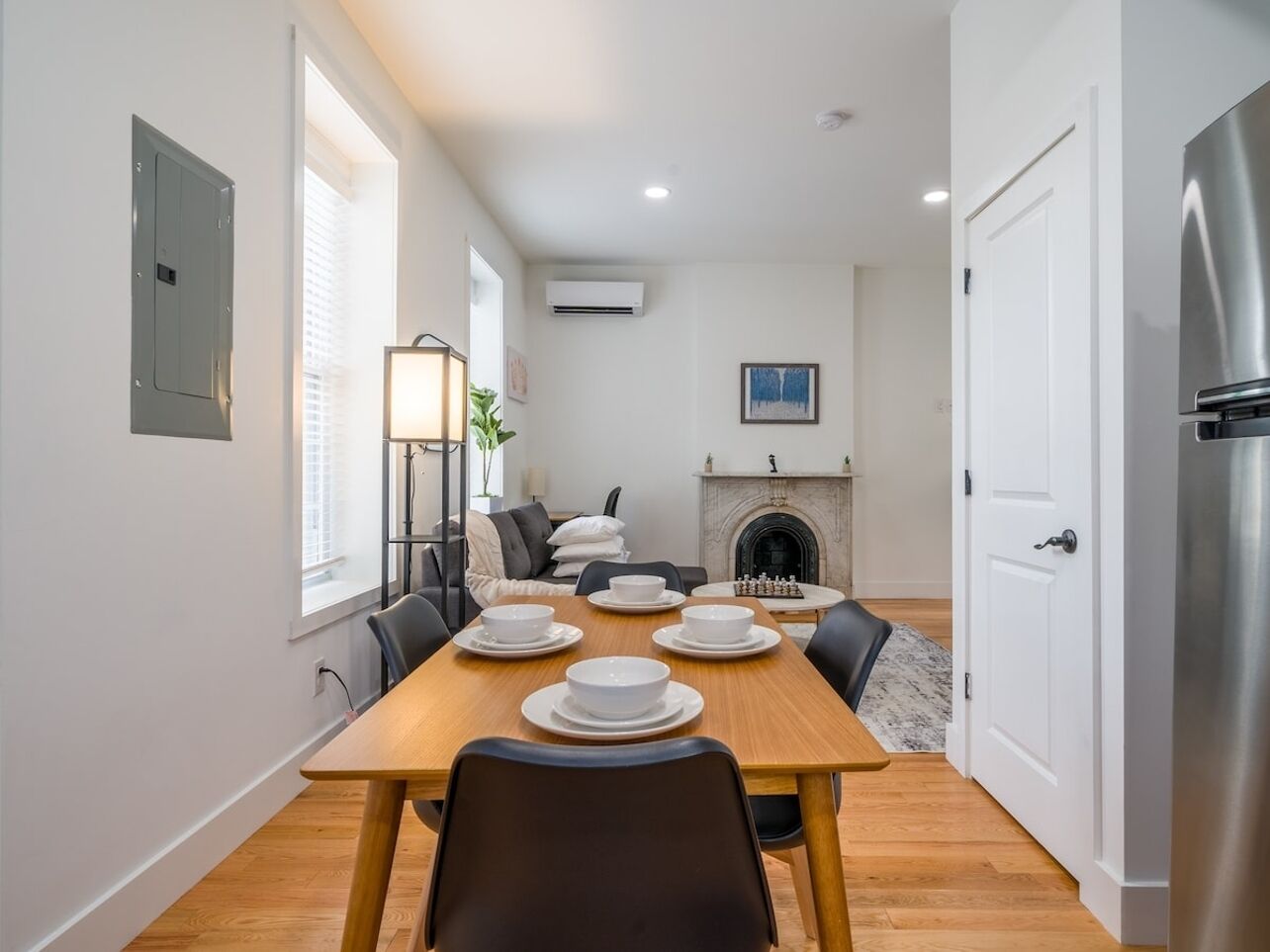 Comedor con mesa de madera dispuesta para cuatro, chimenea y cocina moderna con refrigerador.
