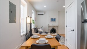 A dining area with a wooden table set for four, a fireplace, and a modern kitchen with a refrigerator. - Cornhill 2BDRM-HighFall+EquippedKitchen+Wi-Fi (Rochester)