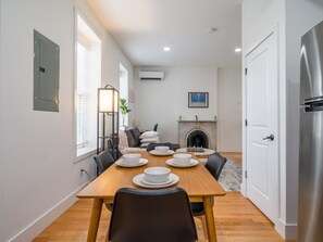 A dining area with a wooden table set for four, a fireplace, and a modern kitchen with a refrigerator. - Cornhill 2BDRM-HighFall+EquippedKitchen+Wi-Fi (Rochester)