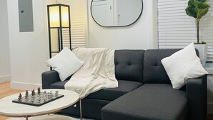 A modern living room with a dark grey sofa, a round coffee table, and a chessboard. - Cornhill 2BDRM-HighFall+EquippedKitchen+Wi-Fi (Rochester)