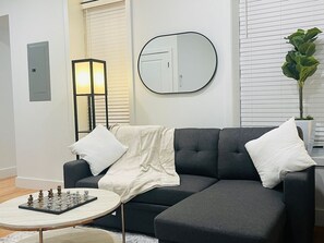 A modern living room with a dark grey sofa, a round coffee table, and a chessboard. - Cornhill 2BDRM-HighFall+EquippedKitchen+Wi-Fi (Rochester)