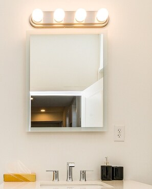 A bathroom with a large mirror, three lights above it, and a sink with two faucets. - Cornhil 1Bed-EquippedKitchen,HighFalls,DT,TV_WiFi (Rochester)