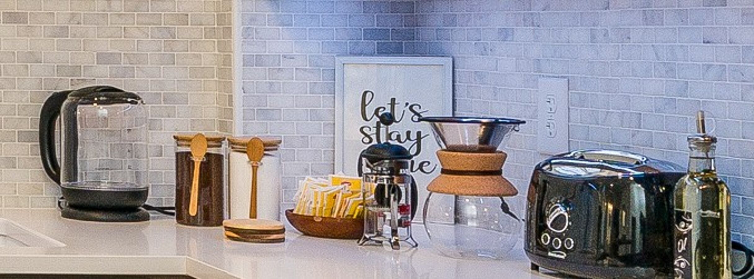 Una encimera de cocina con una cafetera, un hervidor, un tostador, una botella y un cartel que dice "let's stay".