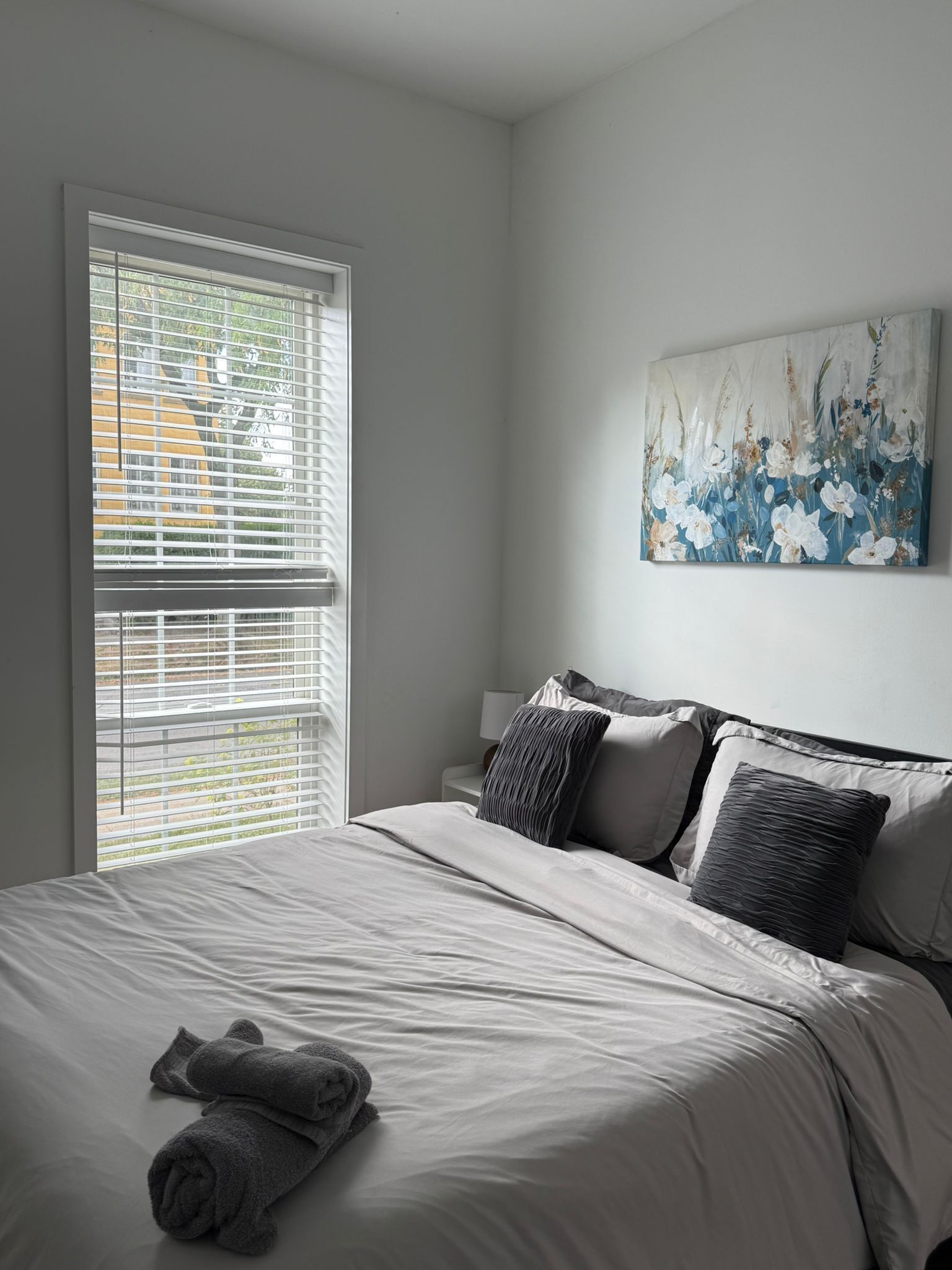 Un dormitorio con una cama grande, una ventana con persianas y un cuadro en la pared.