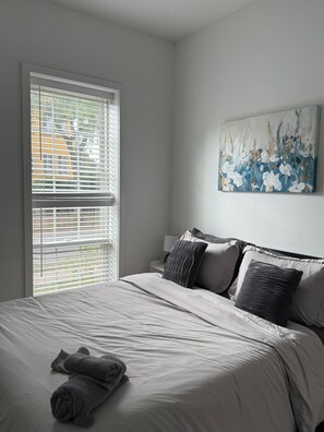 A bedroom with a large bed, a window with blinds, and a painting on the wall. - Cornhil 1Bed-EquippedKitchen,HighFalls,DT,TV_WiFi (Rochester)