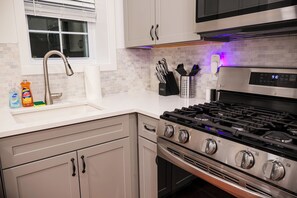 A modern kitchen with a stainless steel stove, a sink, and a window with blinds. - 1BED+EquippedKitchen+HighFalls+TV+DT_Wi-fi (Rochester)