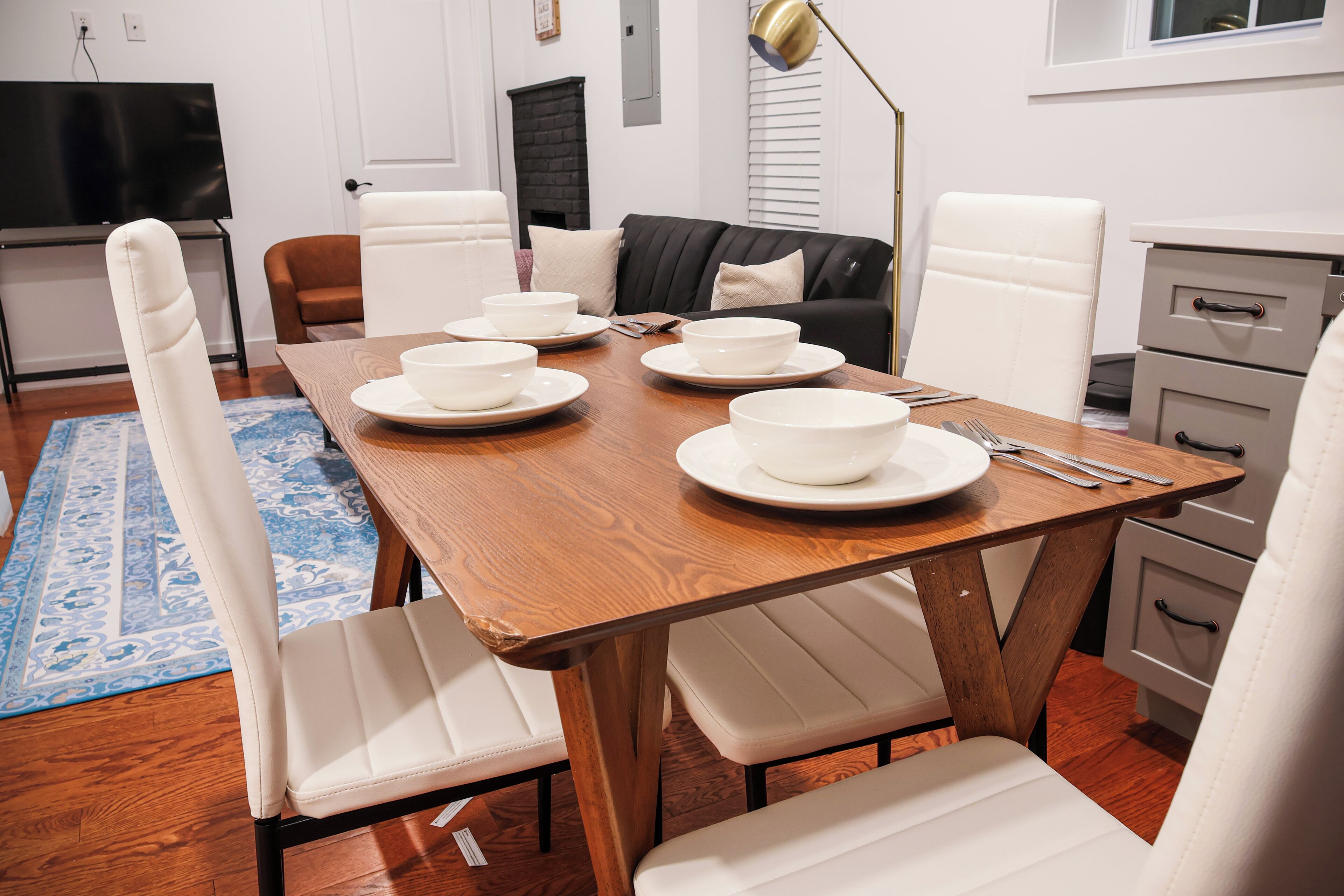 Un coin repas avec une table en bois dressée pour quatre personnes, entourée de chaises blanches.
