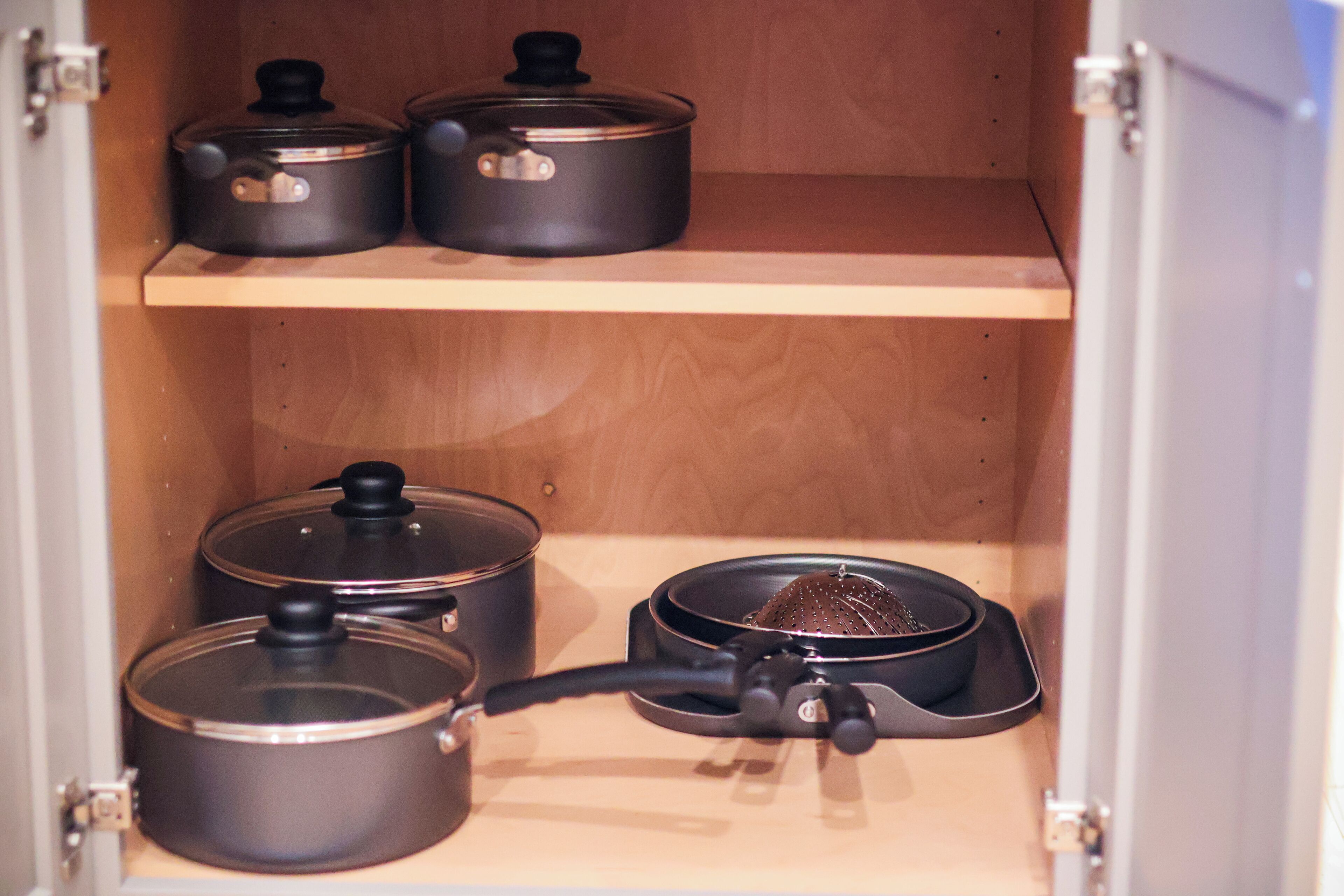 Ein Küchenschrank mit drei schwarzen Töpfen auf der oberen und zwei auf der unteren Ablage.