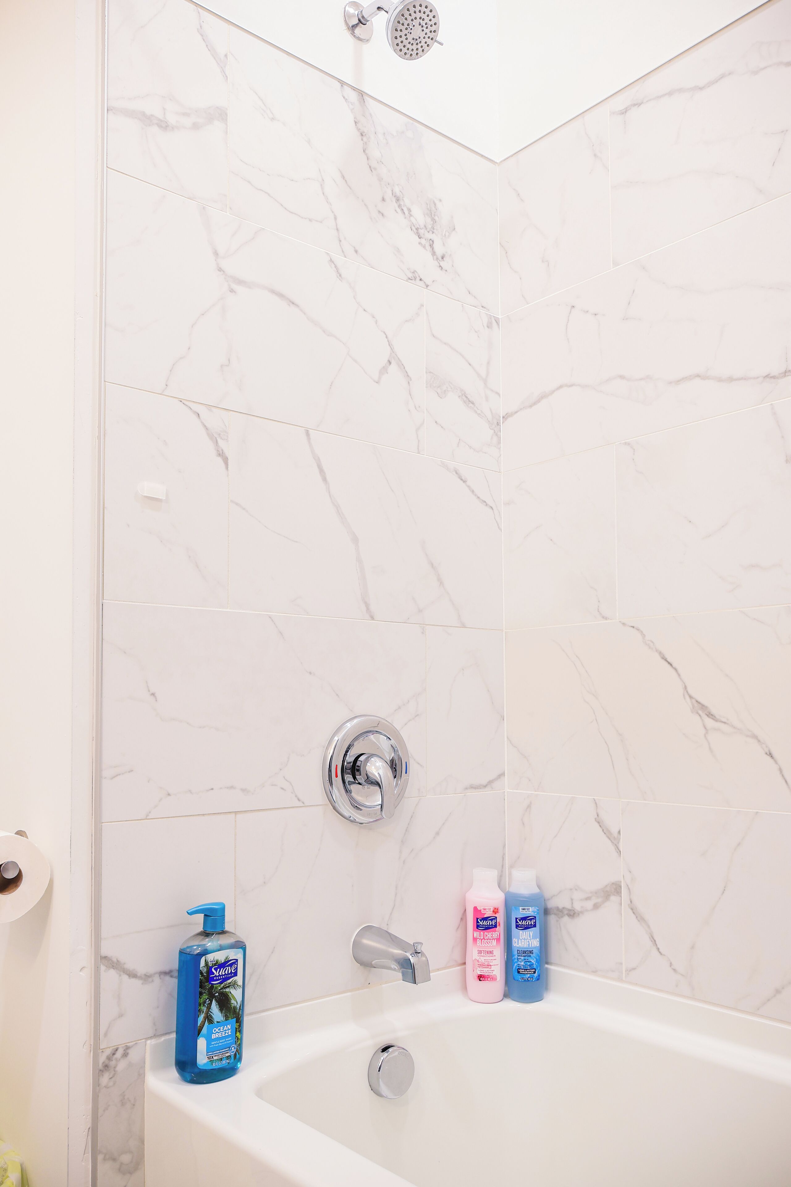 Ein Badezimmer mit weißer Marmorwand, einer Badewanne und zwei Shampoo-Flaschen am Rand.