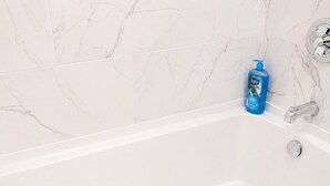 A white bathtub with a chrome faucet, a blue bottle of Soove shampoo, and a hexagonal tile pattern on the floor. - Cozy 1BR with equipped kitchen, dining table, TV, Wi-Fi, near High Falls (Rochester)