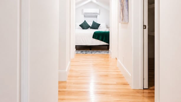 A narrow hallway with wooden flooring leading to a bedroom with a bed, pillows, and a green blanket. - Cozy 1BR with equipped kitchen, dining table, TV, Wi-Fi, near High Falls (Rochester)