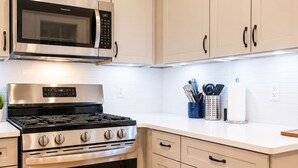 A kitchen with a stainless steel stove, oven, and microwave, light-colored cabinets, and a countertop with kitchen utensils. - Cozy 1BR with equipped kitchen, dining table, TV, Wi-Fi, near High Falls (Rochester)
