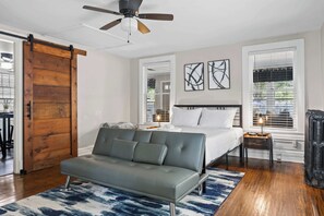Ein Schlafzimmer mit einem Bett, einem grauen Sofa, einem Deckenventilator und einer Holztür.