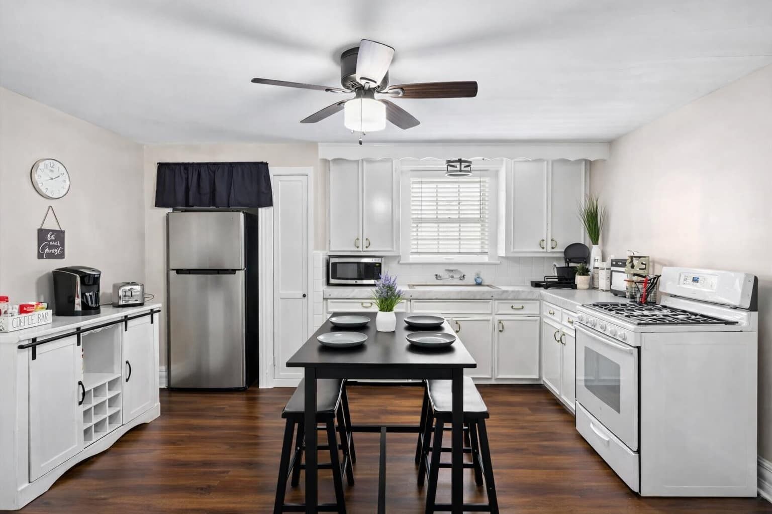 A modern kitchen with white cabinets, a stainless steel refrigerator, a microwave, a stove, and a ceiling fan.