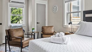 Ein Hotelzimmer mit einem Bett, zwei Stühlen, einem kleinen Tisch mit einer Pflanze und einer Uhr an der Wand.