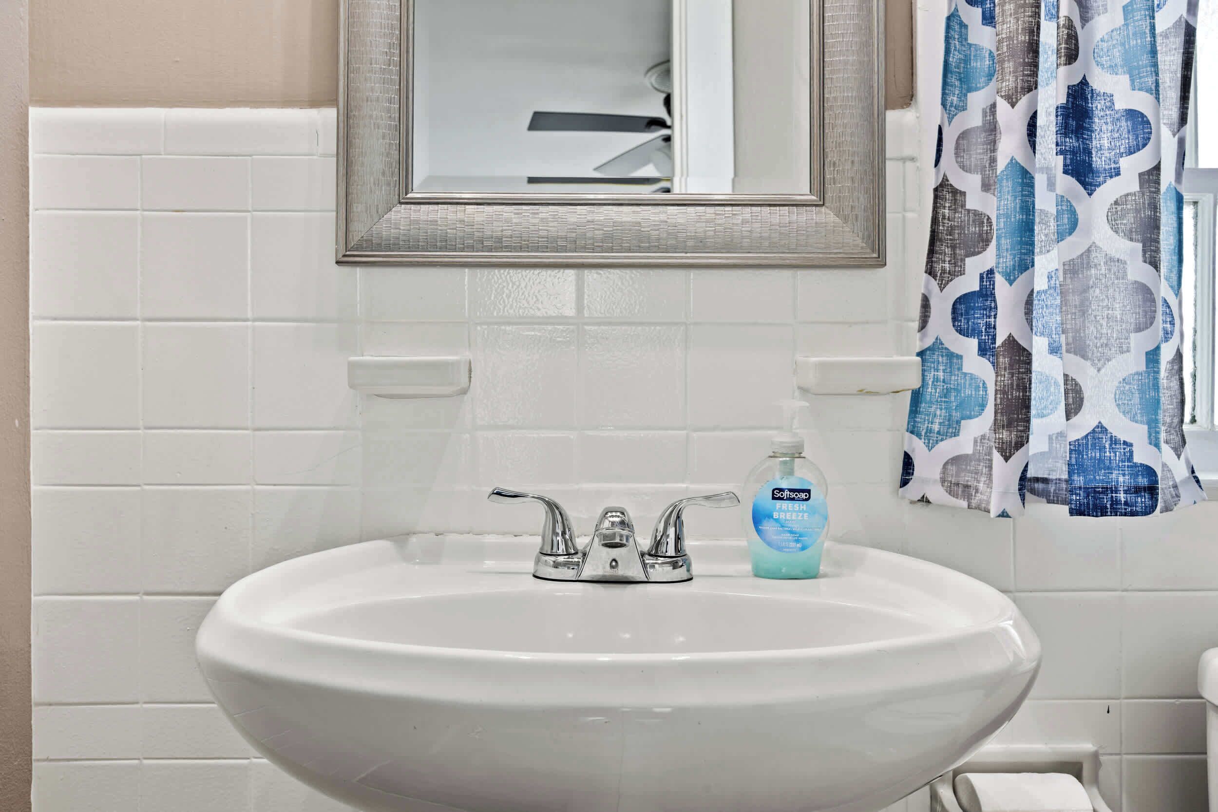 A bathroom with a white sink, a mirror, and a patterned shower curtain.